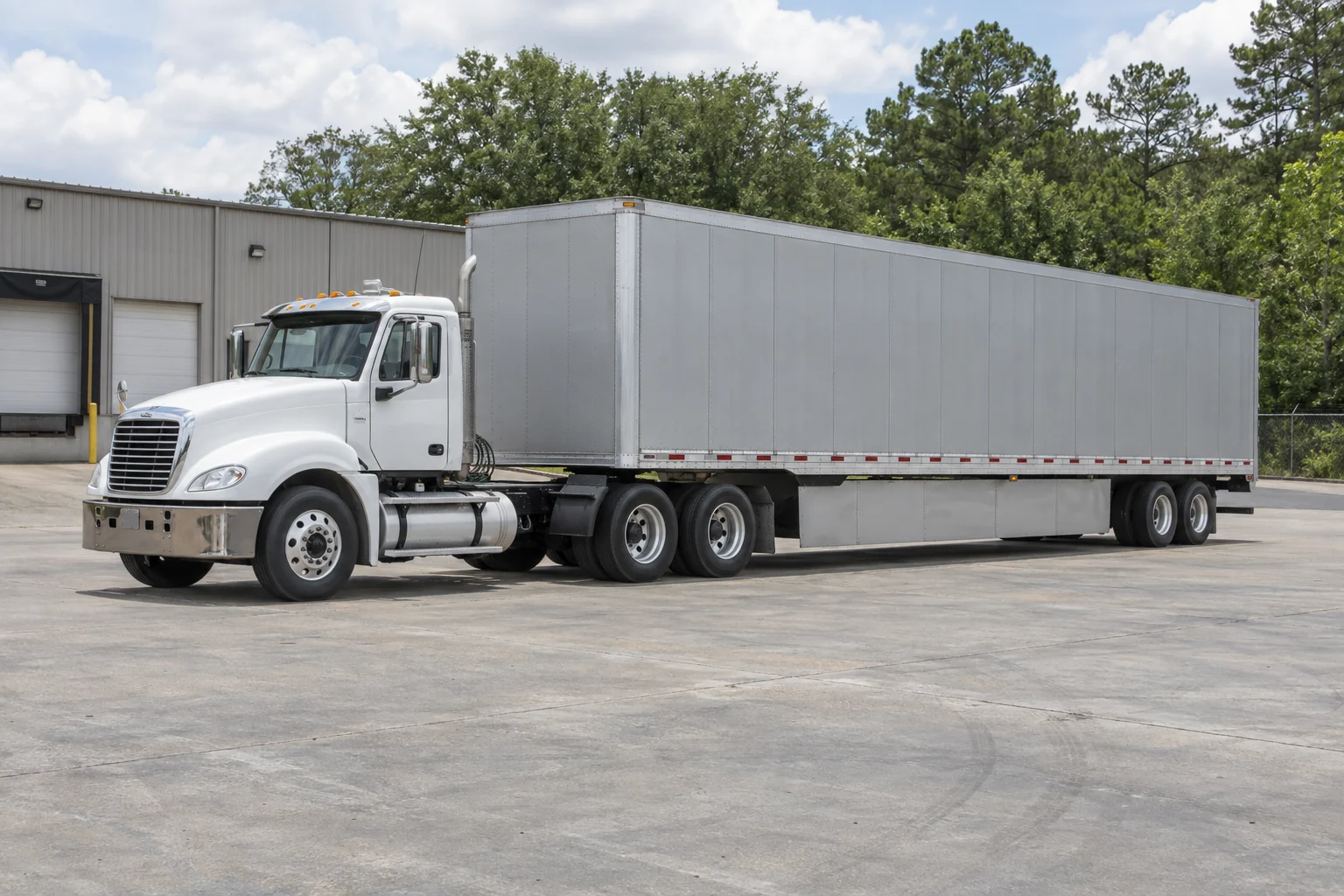 White tractor and silver dry van in a tree-lined industrial yard